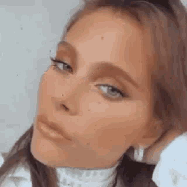 a close up of a woman 's face with a white shirt on and earrings .