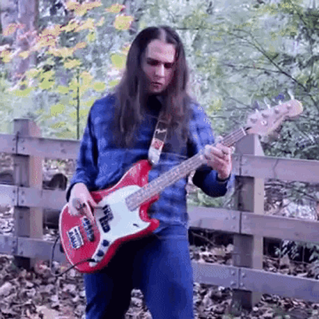 a man with long hair is playing a red electric bass guitar