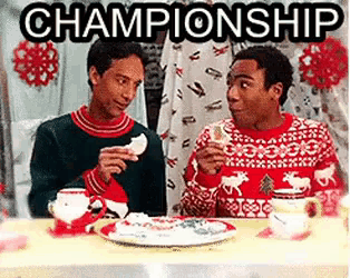 two men in ugly sweaters are sitting at a table eating food and drinking tea .