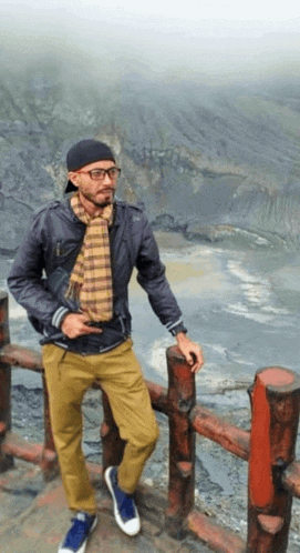 a man wearing glasses and a scarf leans against a wooden railing