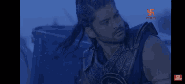 a man with a ponytail is wearing armor and has a subscribe button on the bottom