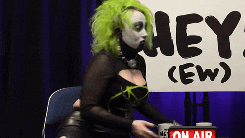 a woman with green hair is sitting in front of a sign that says hey