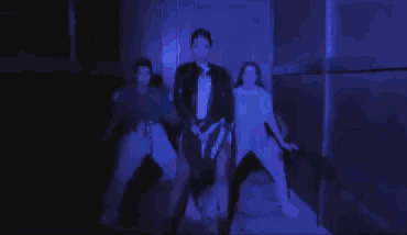 a group of people are dancing in a dark room with purple lights .