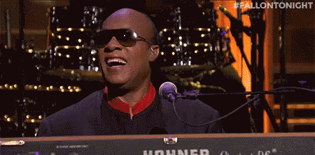 a man in sunglasses is singing into a microphone while playing a keyboard .