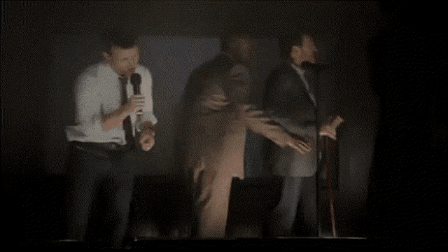 a group of men are standing on a stage holding microphones