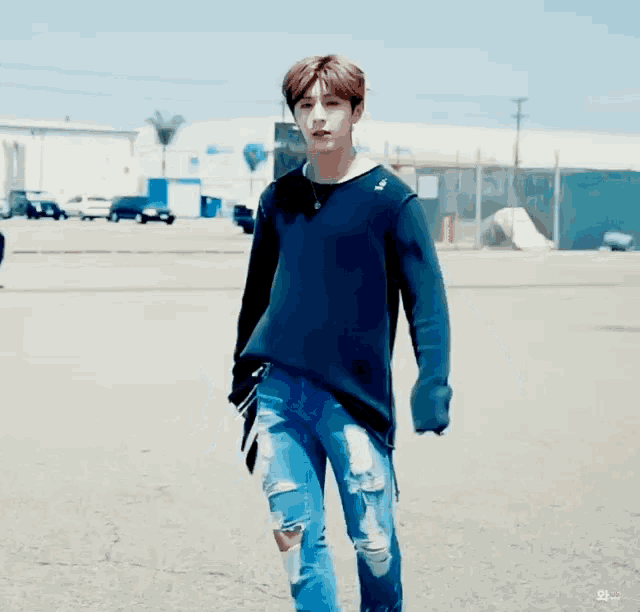 a young man wearing a blue sweater and ripped jeans is walking down the street