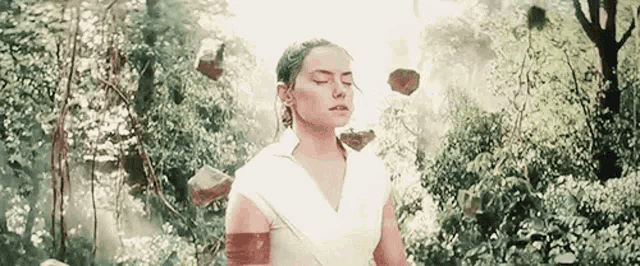 a woman is standing in a forest with her eyes closed and rocks flying around her .