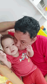 a man in a red shirt kisses a baby in a red shirt with donald duck on it