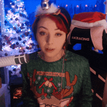 a woman wearing a sweater that says merry christmas is sitting in front of a microphone