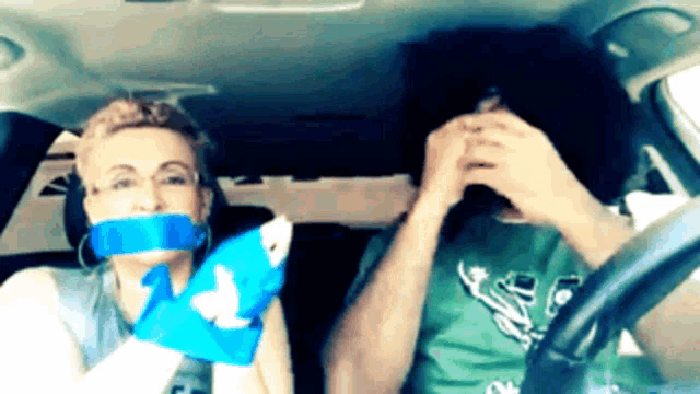 a man and a woman are sitting in a car with duct tape covering their mouths