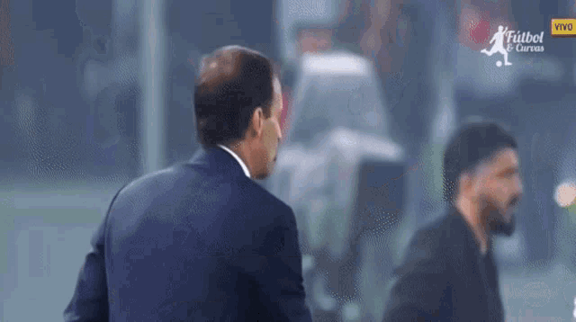a man in a suit stands in front of a screen that says futbol y curvas
