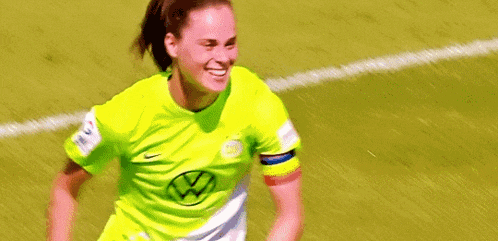 two female soccer players are running on the field and one of them is wearing a yellow jersey .