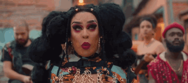 a drag queen with a lot of hair is standing in front of a crowd of people .