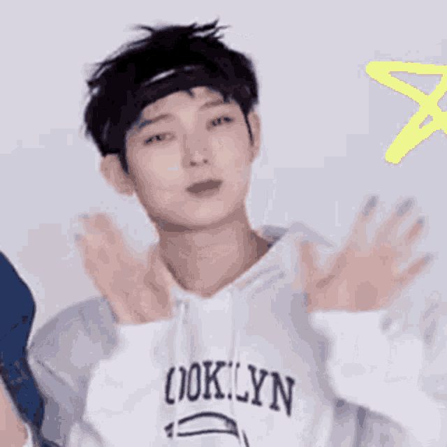a young man wearing a headband and a hoodie is clapping his hands in front of a yellow star .