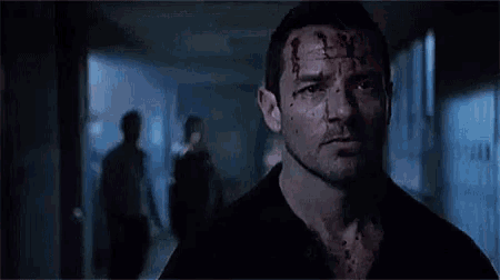 a man with blood on his face is standing in a dark hallway .