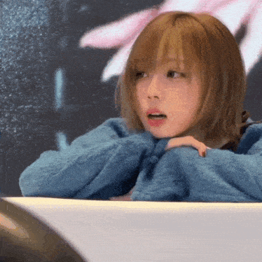 a girl in a blue sweater is sitting in front of a wall
