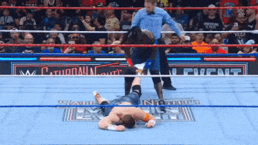 a wrestler is laying on the floor in a wrestling ring while a referee watches