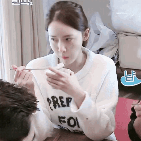 a woman in a white sweater is sitting at a table eating food with a fork .