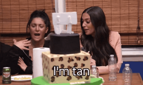 two women sitting in front of a cake that says i 'm tan on it