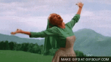 a woman in a green dress is standing in a field with her arms outstretched