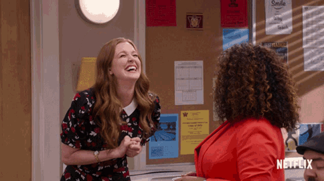 two women are laughing in front of a bulletin board with a poster that says smile
