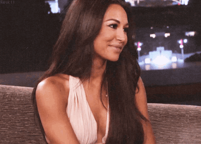 a woman with long dark hair is smiling and wearing a very plunging top