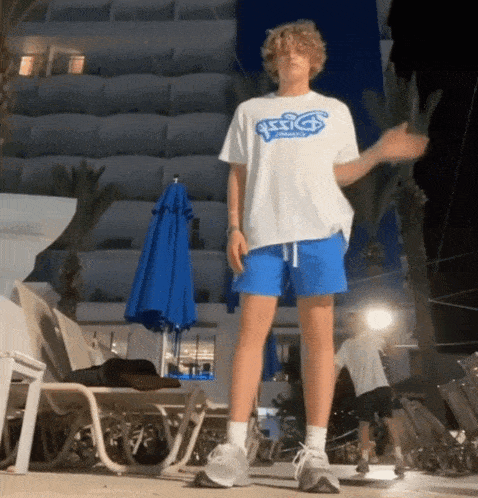 a young man wearing a white asics shirt and blue shorts