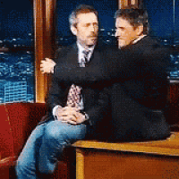 two men are hugging each other while sitting in a chair .
