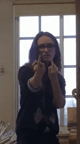 a woman with glasses giving the middle finger in front of a window