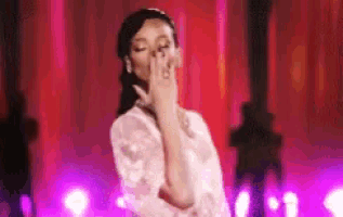 a woman in a white dress is blowing a kiss while standing in front of a red curtain .