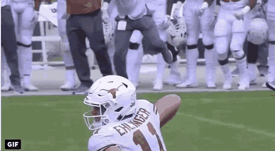 a football player is running with the ball on a field while a group of football players are standing behind him .