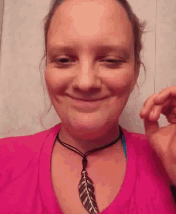 a woman is wearing a pink shirt and a feather necklace .