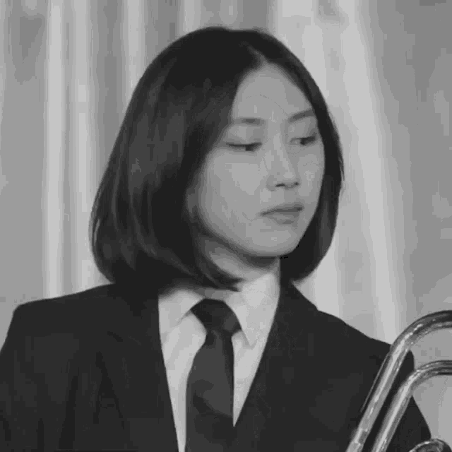 a woman in a suit and tie holds a trumpet