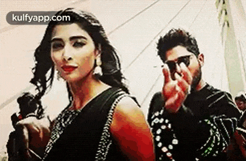 a man and a woman are standing next to each other . the woman is wearing a black saree .