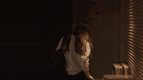 a woman in a white shirt stands in a dark hallway