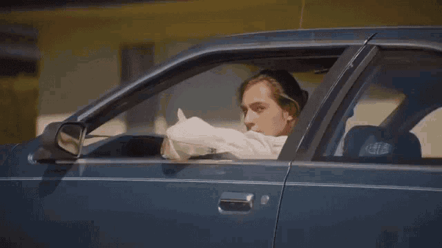 a man is sitting in the driver 's seat of a car holding a tissue .