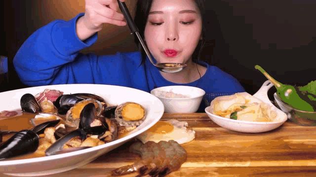 a woman in a blue shirt is eating a large bowl of food with a ladle