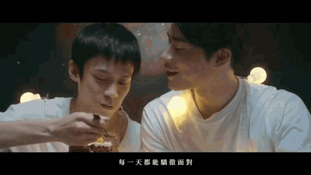 two young men are eating a piece of cake with chinese writing on the bottom right