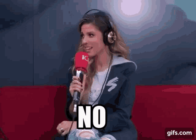 a woman wearing headphones is sitting on a couch holding a microphone and says no .