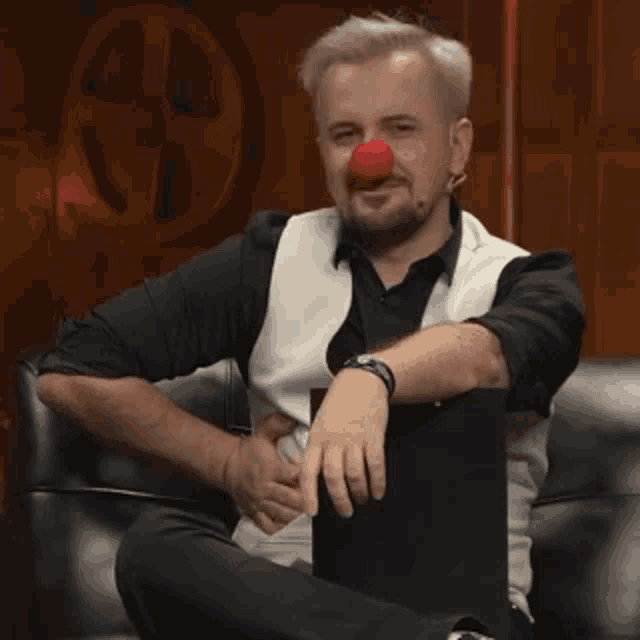 a man with a red nose is sitting on a couch with his hands on his stomach .