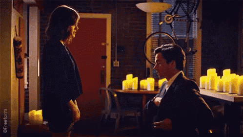 a man is kneeling down to propose to a woman in a room with candles