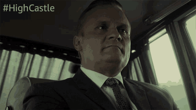 a man in a suit and tie is sitting in a car with the hashtag #highcastle behind him