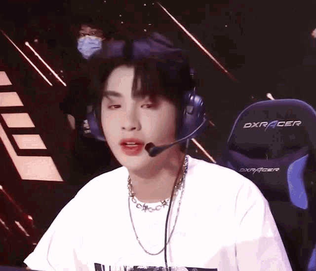 a man wearing headphones and a necklace is sitting in front of a dxracer chair