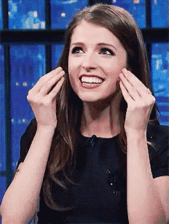 a woman in a black dress is making a funny face with her hands on her face .