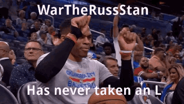 a basketball player is sitting in the stands at a basketball game with his hands in the air .