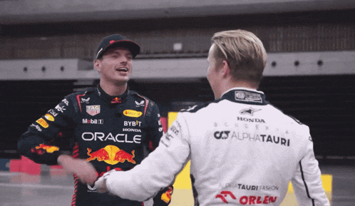 two men shaking hands with one wearing a red bull shirt