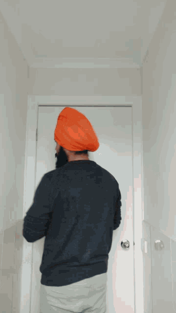 a man wearing an orange turban is standing in front of a white door