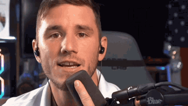 a man is talking into a microphone while wearing headphones and a white shirt .