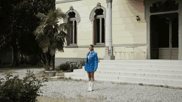 a woman in a blue jacket and white boots is standing in front of a yellow building
