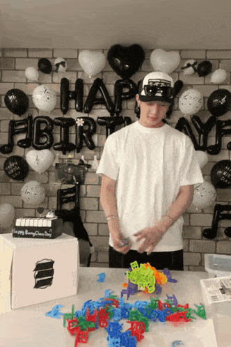a man standing in front of a wall with balloons and a cake that says happy birthday